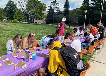 Students sit at tables outdoors on the SUNY JCC Jamestown campus and tie dye shirts.