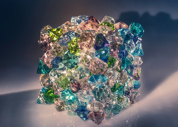 A cube comprised of many different pieces of glass in multiple colors glistens in light.