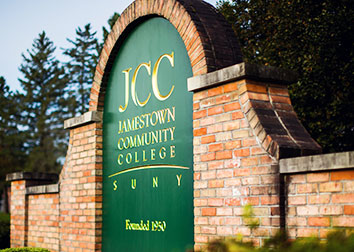 An arching brick wall frames the green sign emblazoned with gold letters, welcoming all to Jamestown Community College.