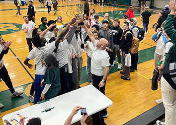 Students in the Physical Education Complex at SUNY Jamestown Community College celebrating their pep rally and holding up a trophy as onlookers take pictures with their cell phones.