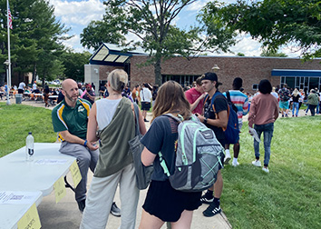 A man leans against a table while speaking with students at an Involvement Fair on the SUNY JCC Jamestown campus.