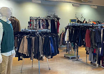 A mannequin stands in front of circular racks of clothing in a store-like room.