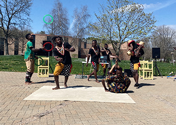 A group of acrobats perform on a sidewalk with trees in the background.