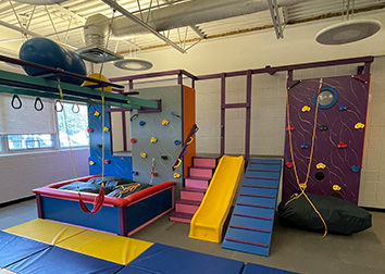 A gym with fitness balls, rings, swings, a pit, stairs, a slide, and a climbing wall.