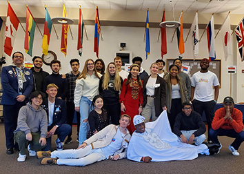A group of students pose under the international flags in the Student Union at SUNY Jamestown Community College.