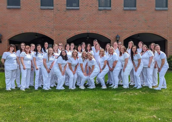 A group of nurses pose together outside of a brick building.