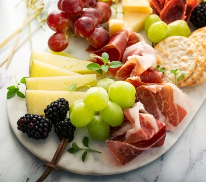 Charcuterie board holding fruit, meats, cheeses, and crackers.