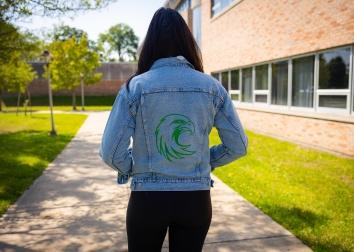 A student on campus wearing a denim jacket with a sparkly Jayhawk graphic on the back.