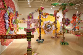 Colorful, intricate art installation featuring large geometric structures and patterns made from various materials. The room is vibrant and visually dynamic.
