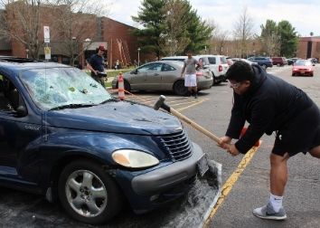 A student wearing goggles uses a sledge hammer to smash a PT cruiser.