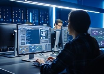 A person scrolls on a computer monitor with additional computers in the background.