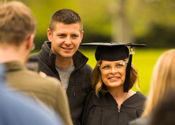 An image of a parent who is graduating, with her son standing at her side.