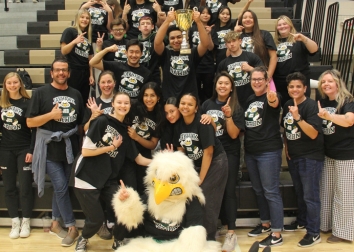 A group of people pose for a picture with the SUNY JCC mascot after winning a trophy at their pep rally.