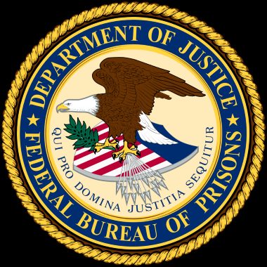 Circular gold-edged seal of the U.S. Department of Justice Federal Bureau of Prisons, featuring an eagle, shield, arrows, and olive branch.