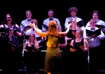 A person conducts a choir of people holding folders