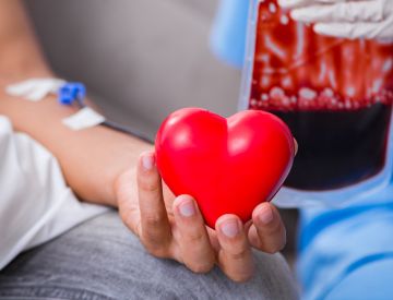 A person's hand holding a heart shape squish item while they are donating blood.