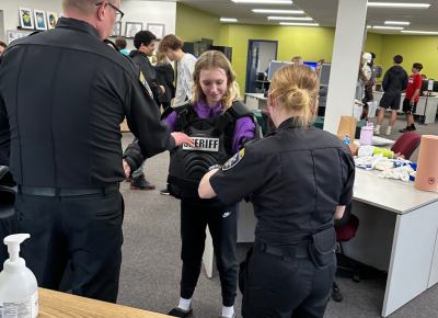 A young student at a career fair gets help trying on a sheriff vest with help from sheriff personnel.