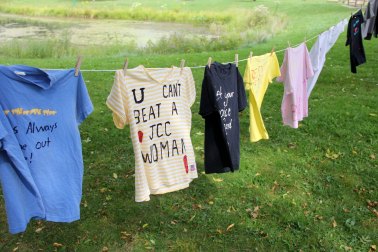 T-shirts hang drying on a clothesline outdoors in a grassy yard with a pond in the background.