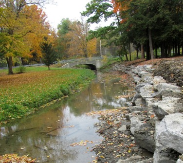 A tranquil scene featuring a small stone bridge over a calm creek, surrounded by vibrant autumn foliage.