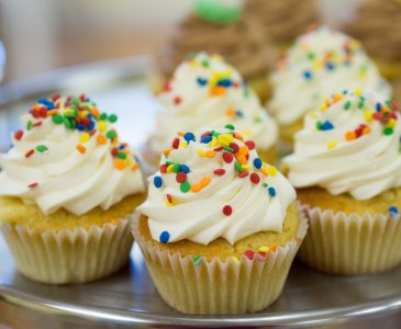 A tray of yellow cupcakes with white icing and colorful sprinkles.
