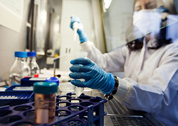 A person wearing a mask while holding beakers containing liquid