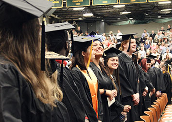 Students wearing graduation caps and gowns stand together at a commencement ceremony.