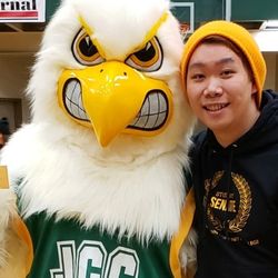 A student standing with JJ Jayhawk in the gymnasium