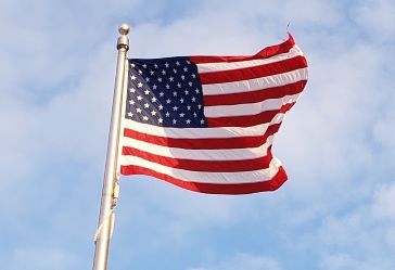 An Amerian flag waving in the win with a clear blue sky in the background.