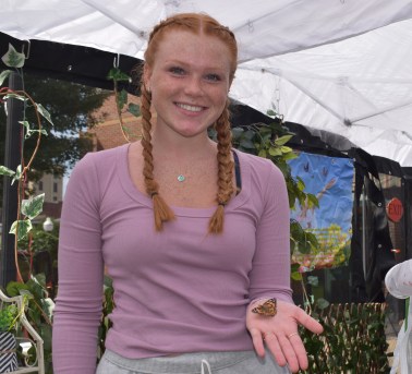 Smiling young person with braided red hair holds a small butterfly on their open palm.