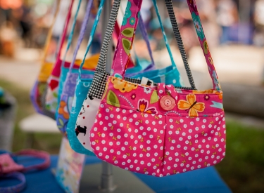 A collection of brightly colored, handmade fabric purses hang in a row, with a pink and white polka dot purse in the foreground.