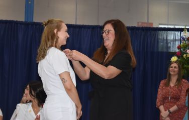 A college professor attaches a pin to the shirt of a graduating nursing student.