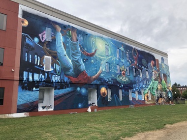 The side of a building where a colorful mural is being painted.