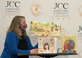 Woman standing in front of a backdrop reading a book out loud to an audience.