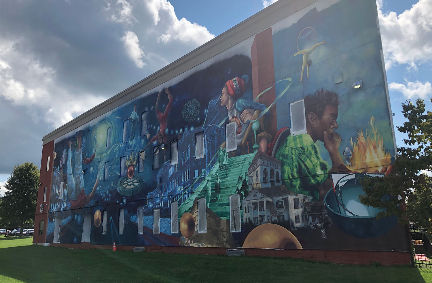 mural on the side of LLAC building on JCC's Cattaraugus County Campus depicting colorful themes of people, buildings, and space with abstract backgrounds