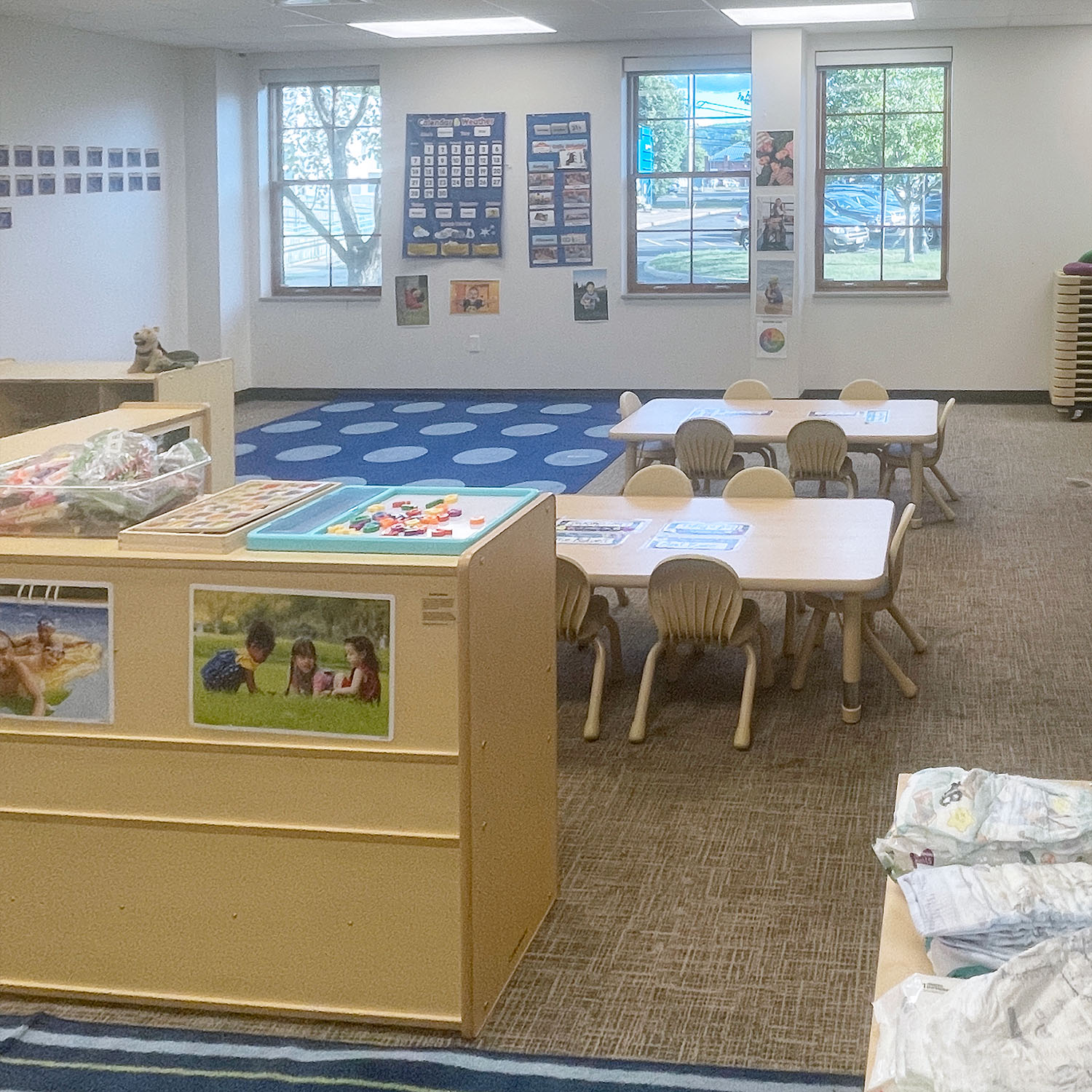 Room in JCC's Early Learning Center, featuring tables, shelves, and playmats for children, with posters on the wall
