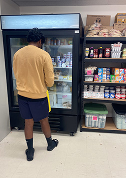 A student stands in front of a cooler with glass doors in a food pantry.