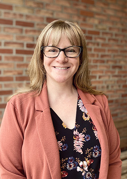 A woman wearing glasses standing in front of a brick wall.