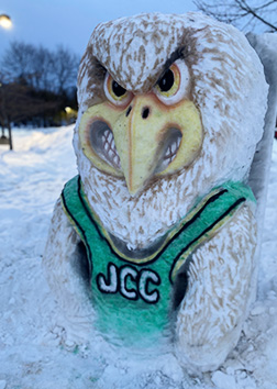 SUNY Jamestown Community College mascot, JJ Jayhawk, painted on a mound of snow.