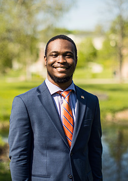 A man wearing a suit standing outdoors on a sunny summer day.