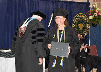 A woman holding a degree walking past a man, both in caps and gowns.