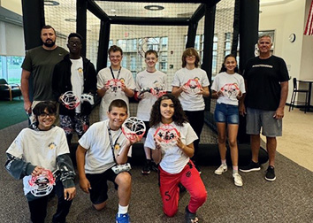 A group of students hold drones and pose with their drone soccer coaches.