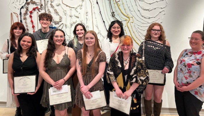 Ten people, many holding certificates of achievement, pose together in an art gallery.