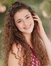 An image of a young woman smoothing her wavy hair while standing outdoors.