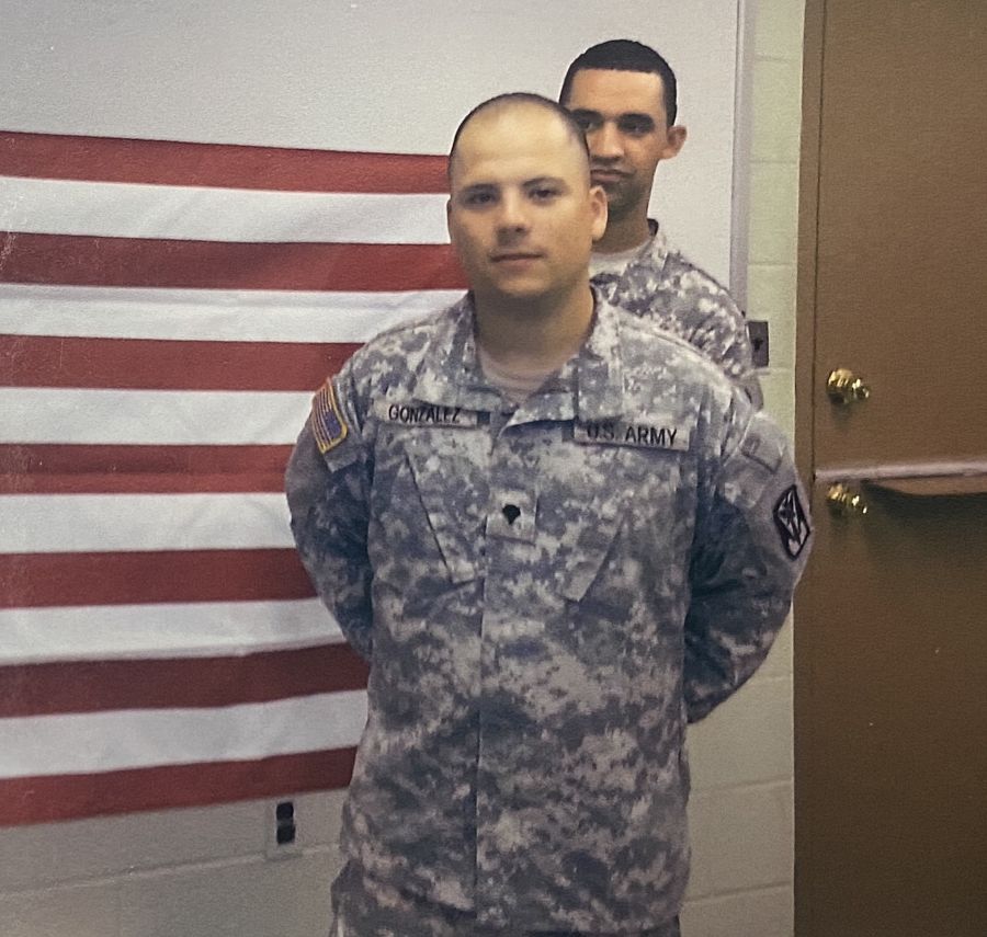 A member of the Army poses in uniform with red and whites strips from the U.S. flag in the background.