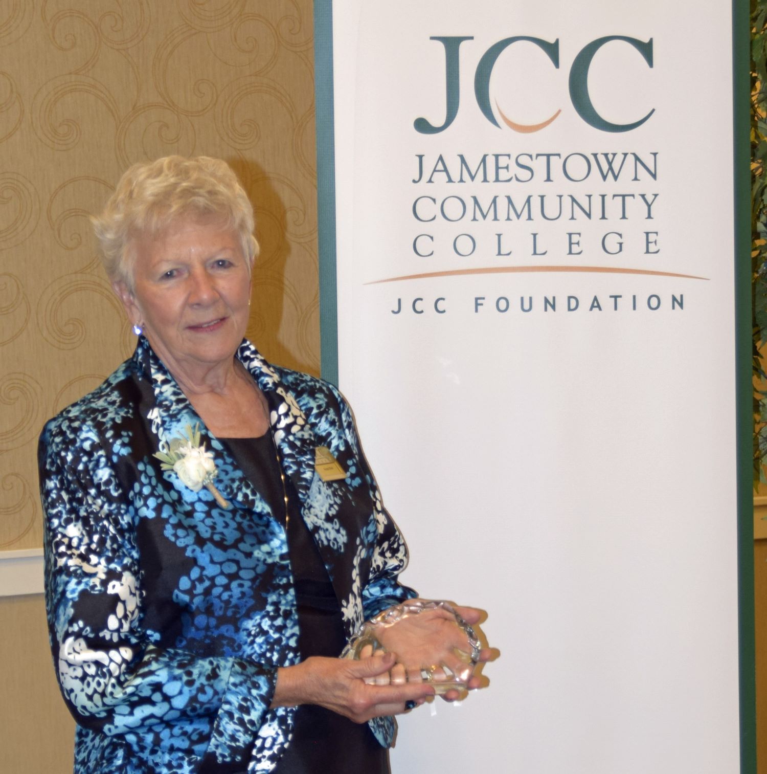 Donna Beal poses while holding the glass John D. Hamilton Award with a JCC Foundation background.