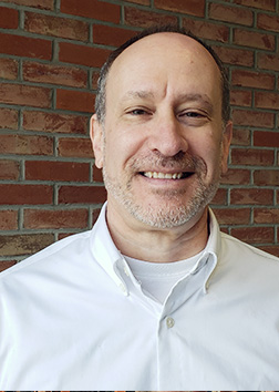 A man in a collared shirt standing in front of a brick wall.
