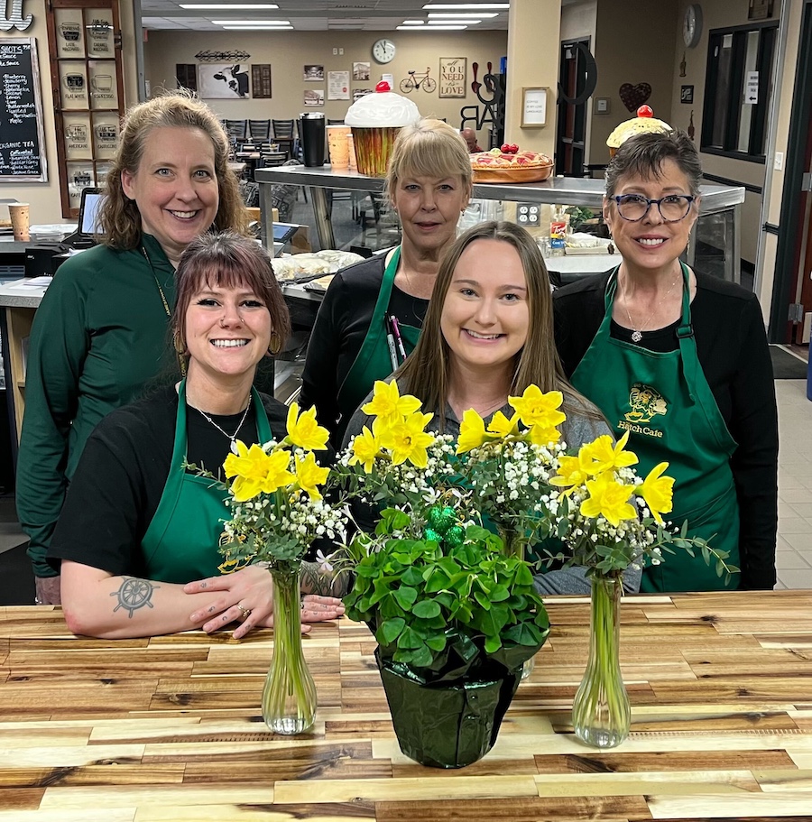 Cafe staff pose together with flowers in a bakery area.