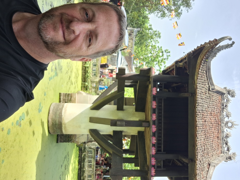 Man in selfie style pose with One Pillar Pagoda in Hanoi, Vietnam in the background.