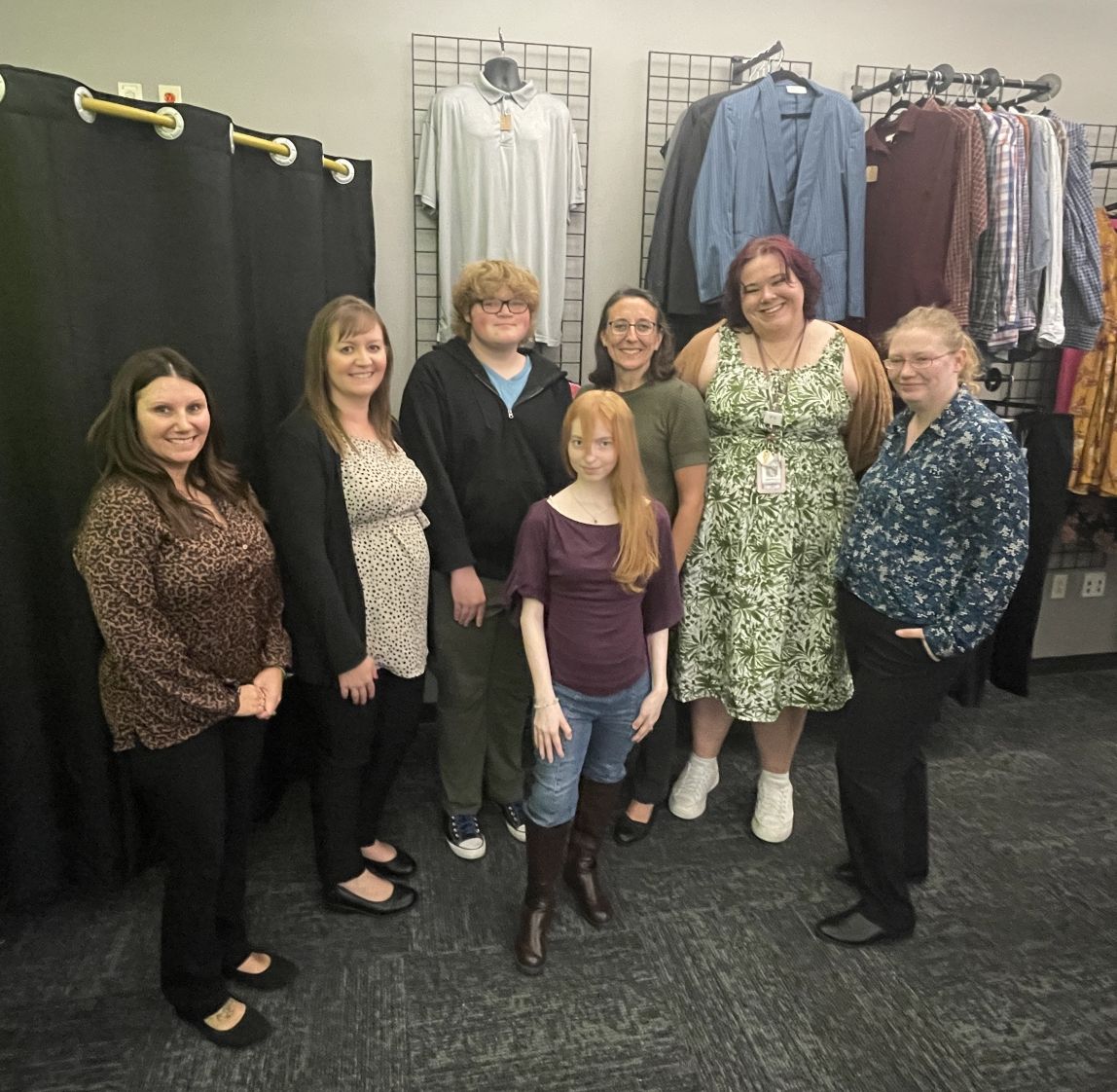 Group of seven individuals standing in front of racks of clothing.