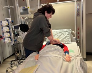A young man gives chest compressions to a dummy lying in a hospital bed.
